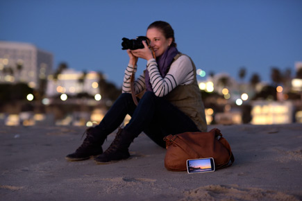 Take control of your camera Photo of a woman taking a photo while her smartphone sits nearby, with an image on the LCD