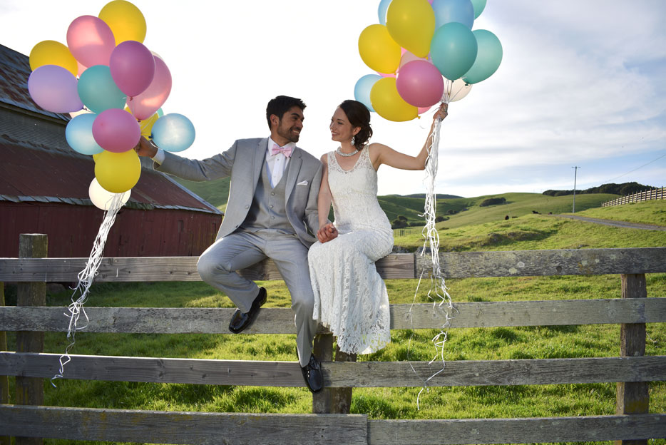 Nikon D3400 photo of a bride and groom sitting on a fence holding colorful balloons