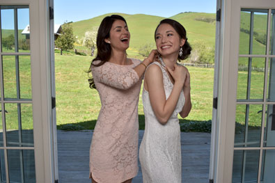 Photo of a woman putting a necklace on a bride's neck