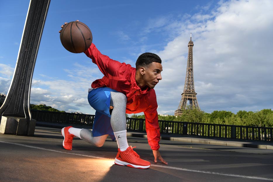 D850 DSLR photo of a basketball player kneeling with the ball in his hand and the Eiffel Tower in the background