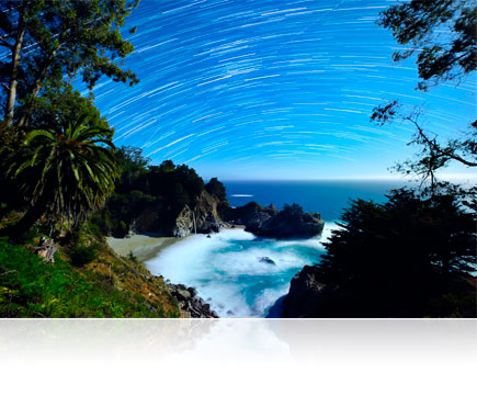 Time lapse photo of the stars in the night sky above a tropical island landscape in low light