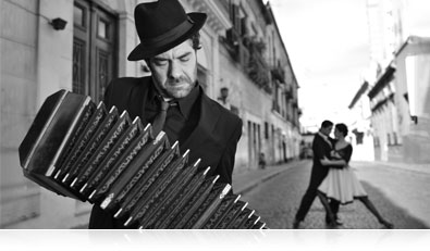 B&W photo of a musician with tango dancers in the street beyond