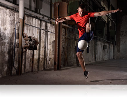 Photo of a soccer player in a run down building kicking a ball in air, lit with the Nikon SB-500 Speedlight flash