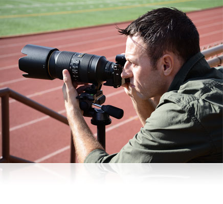 Photo of a man with the Nikon 1 V3 held up to his eye, and the camera on a tripod, shooting track and field