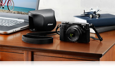 Photo of the Nikon 1 V3, its case, a laptop and accessories on a desk