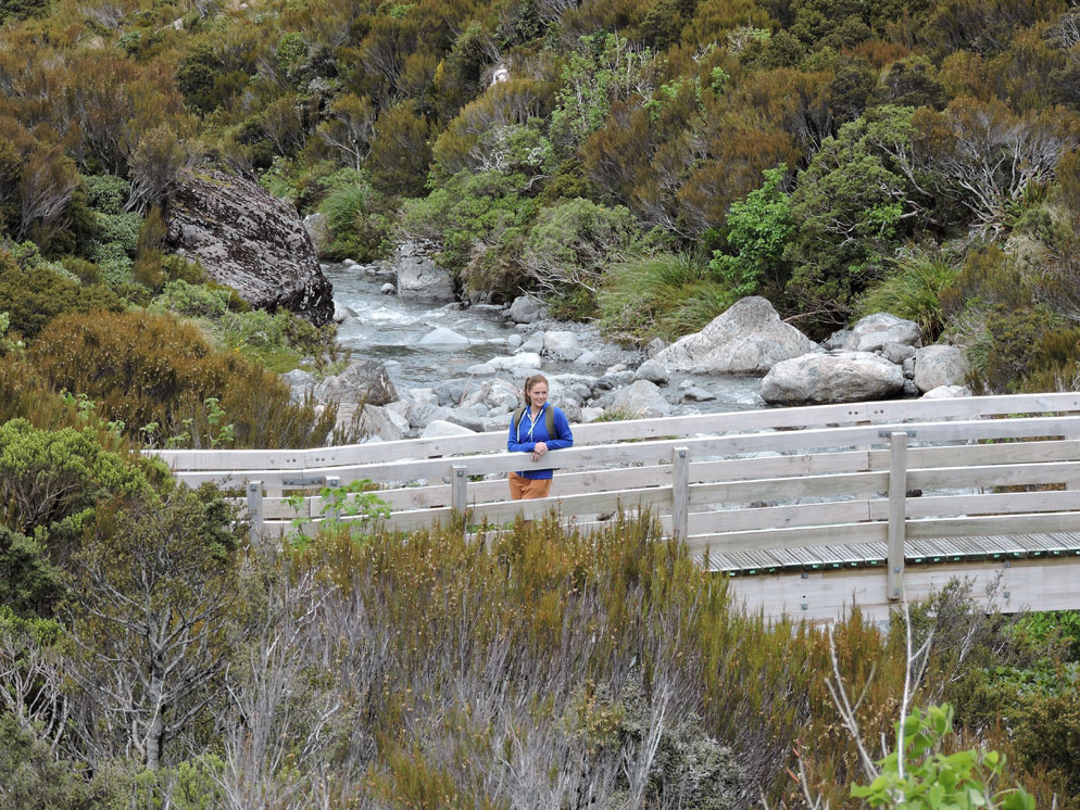 Zoom slider - rugged mountain landscape with a woman standing on a wood bridge