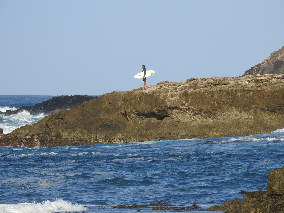 Zoom slider photo of a rocky shoreline and a surfer on the rocks, zoomed in tighter