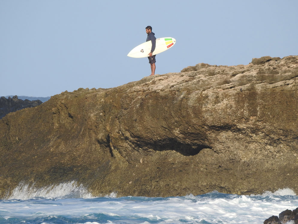 Zoom slider photo of a rocky cliff and a surfer on the rocks, zoomed in with water at the cliff base