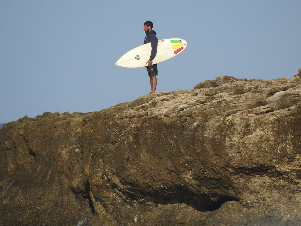 Zoom slider photo of a rocky cliff and a surfer on the rocks, zoomed in all the way