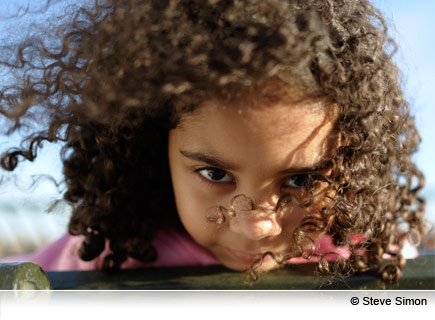 Complete control, even in low light Portrait of curly haired girl looking at the camera taken with the AF-S NIKKOR 28mm f/1.8G lens.