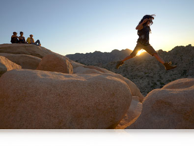 Fotografia tirada com uma Nikon D7000 de uma pessoa pulando entre grandes rochas com um grupo de pessoas assistindo à distância com inserção de exemplo do alcance de ISO da câmera