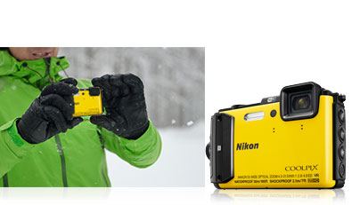 Photo of a person in a green ski jacket in the snow holding the yellow COOLPIX AW130 and the camera inset next to the photo