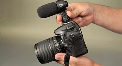 Learn about video accessories at Nikon School Photo of a person's hands holding a Nikon D-SLR with the ME-1 mic on the hotshoe