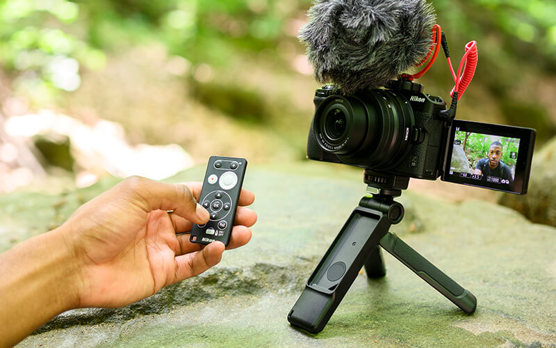 Photo of the Z 30 mirrorless camera on the tripod grip, with a person's hand holding the ML-L7 remote control