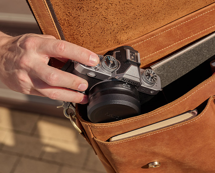 NIKKOR Z 26mm f/2.8 lens on a Z fc, photo of a person putting it into a satchel