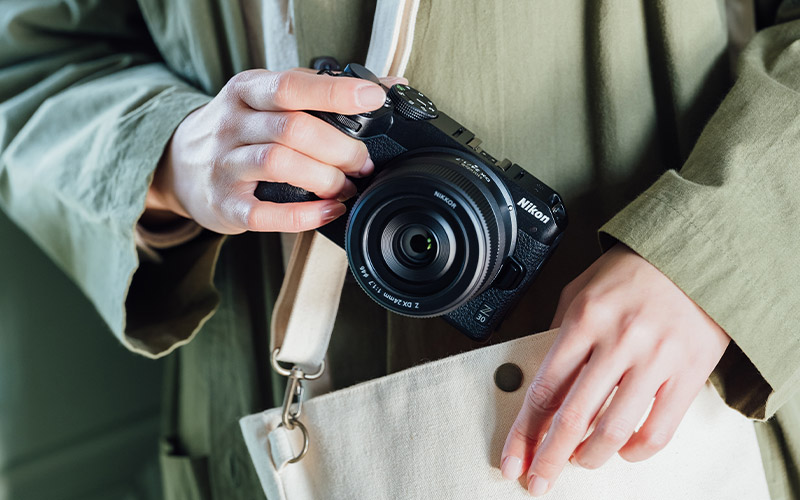 photo of a woman pulling a camera and NIKKOR Z DX 24mm f/1.7 lens from a purse
