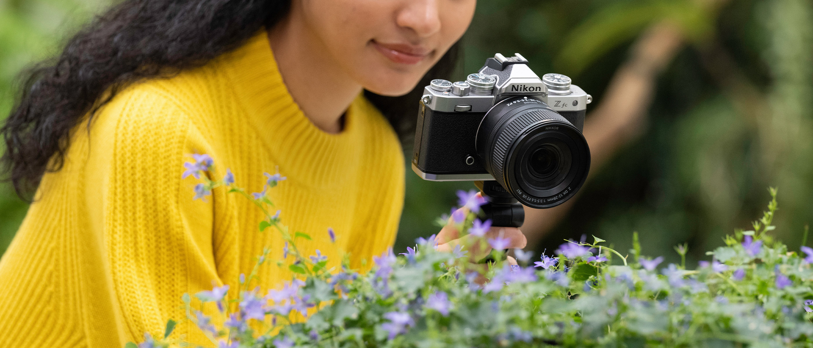 photo of a woman in a yellow sweater with a Z fc and NIKKOR Z DX 12-28mm f/3.5-5.6 PZ VR photographing flowers