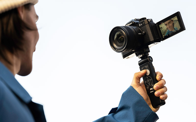 photo of a man in a blue jacket holding the NIKKOR Z DX 12-28mm f/3.5-5.6 PZ VR on a camera and handheld grip, with him on the LCD