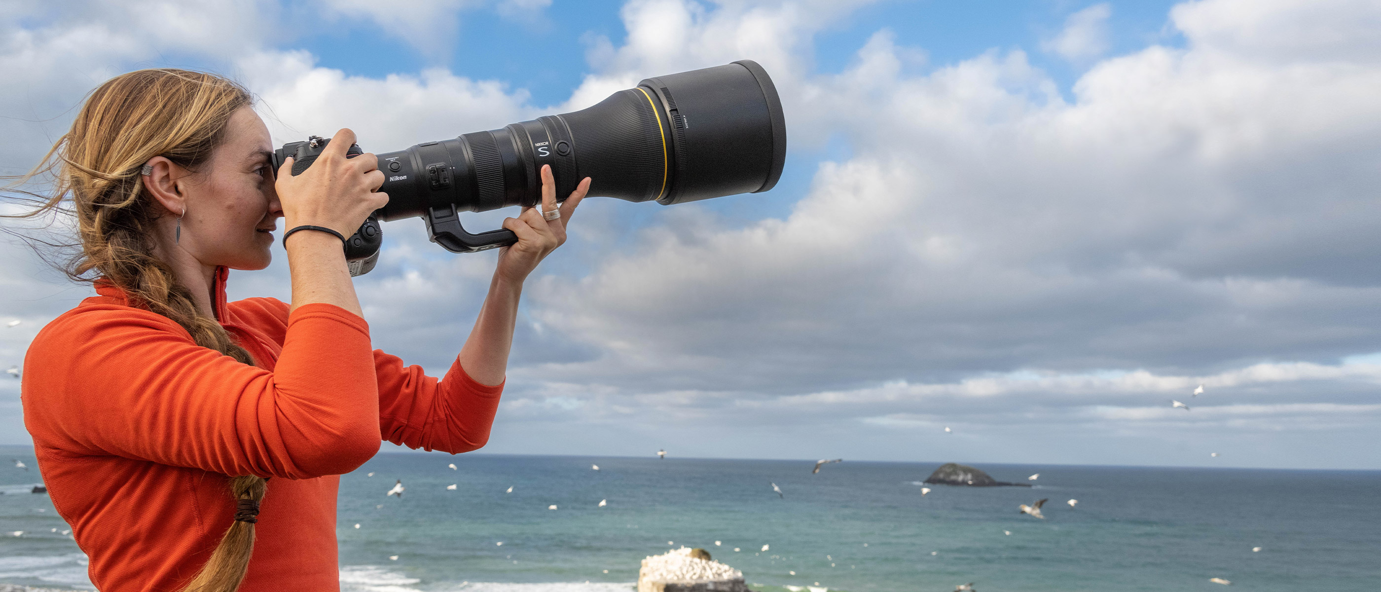 Photo of a woman in an orange shirt holding a Nikon camera with the NIKKOR Z 800mm f/6.3 VR S lens attached photographing birds