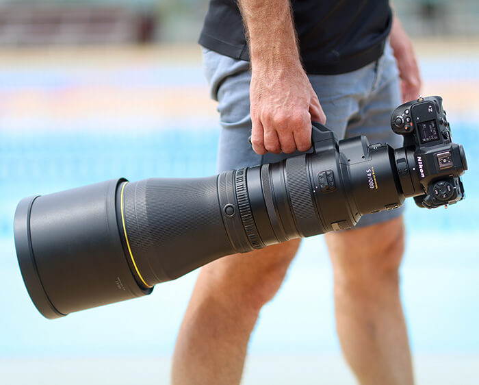 photo of a person walking with the NIKKOR Z 600mm f/4 TC VR S on a camera in hand