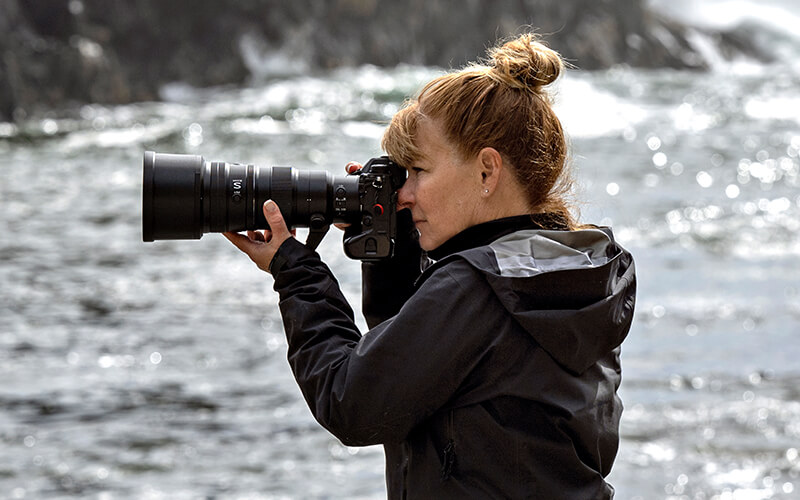 Photo of a woman photographer shooting with the NIKKOR Z 400mm f/4.5 VR S in profile with water in the background