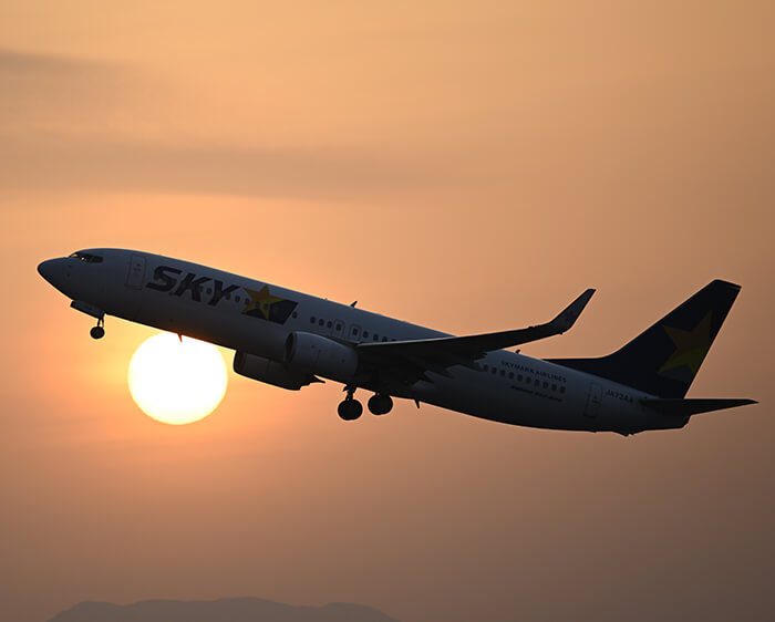 NIKKOR Z 400mm f/4.5 VR S photo of a jet plane in flight with the setting sun behind, in an orange sky