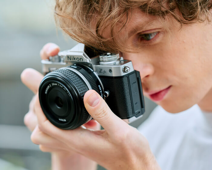 Model holding the Z fc and NIKKOR Z 28mm f/2.8 (SE) up to their eye