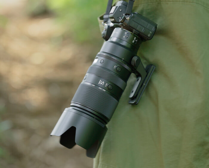 photo of the NIKKOR Z 100-400mm f/4.5-5.6 VR S lens on a Z camera, held by a photographer, pointing downward