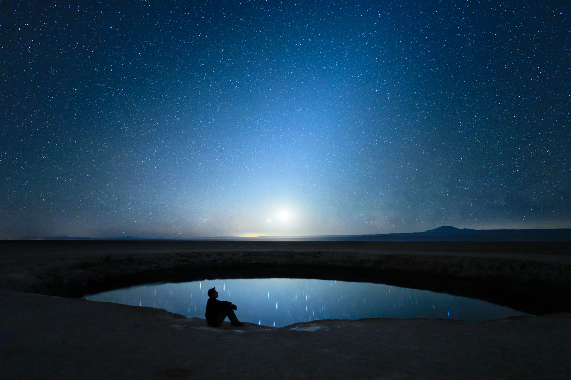 night photo of a starry sky and reflection in a pond, with a figure in silhouette starring at the sky, taken with the NIKKOR Z 20mm f/1.8 S