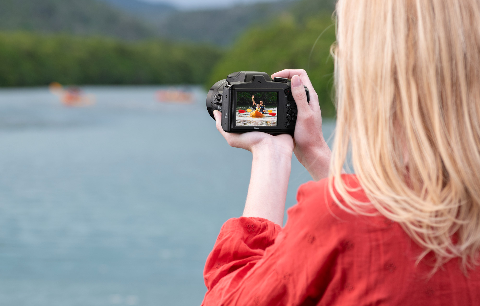 Photo of a woman holding the Nikon COOLPIX B600 in her hands with a kayaker on the LCD