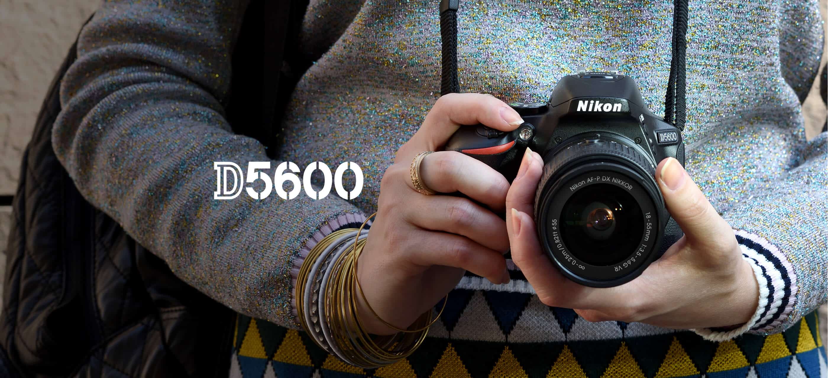 Woman holding Nikon D5600 black camera with 18-55mm zoom lens