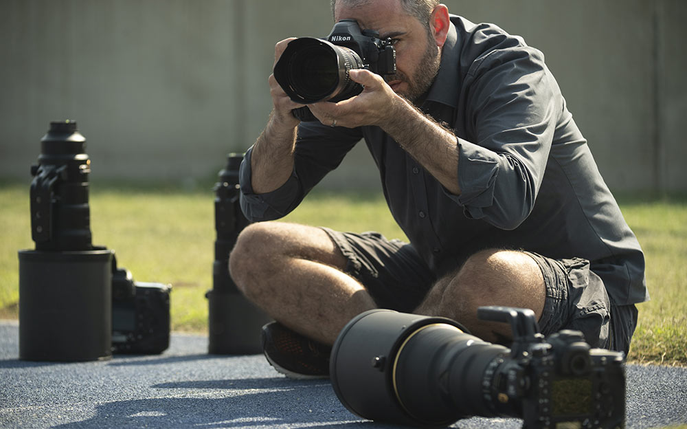 Photo of a photographer sitting on the ground shooting with cameras and lenses next to him