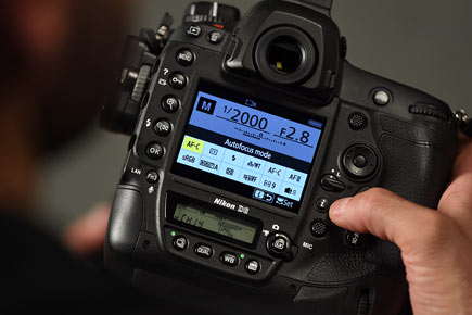 Photo of the D6 DSLR in the hands of a photographer, with info on the LCD