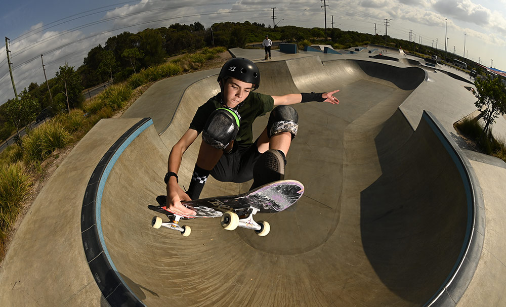 D6 DSLR photo of a skateboarder in air above a skatepark bowl