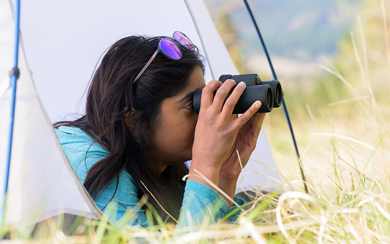 photo of a young woman looking through PROSTAFF P3 binoculars from inside a tent