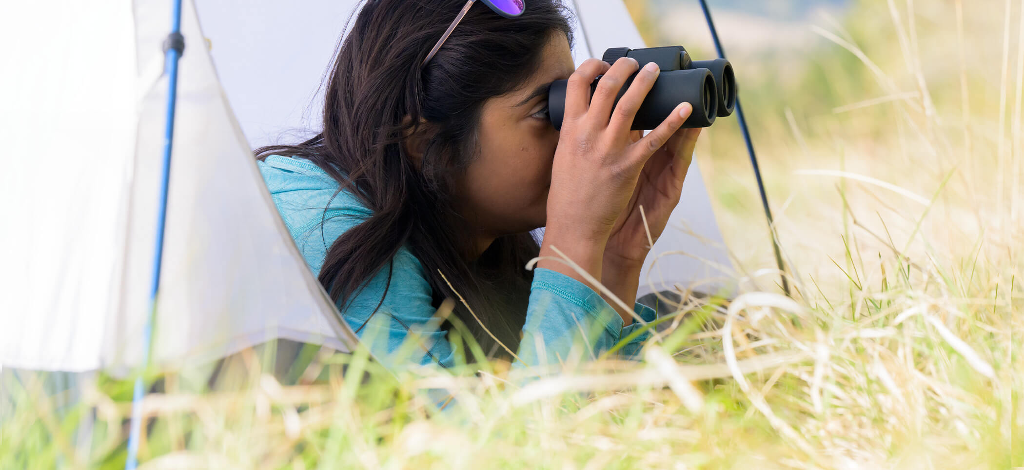 Photo of a woman in a tent, looking through a pair of PROSTAFF P3 binoculars