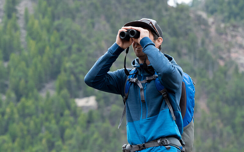 a man in a blue jacket outdoors looking through binoculars