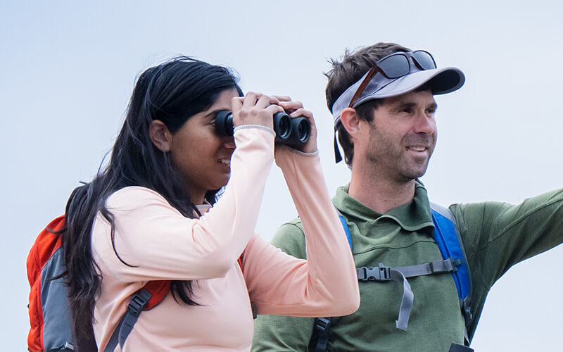 photo of a man and woman outdoors, she is looking through binoculars