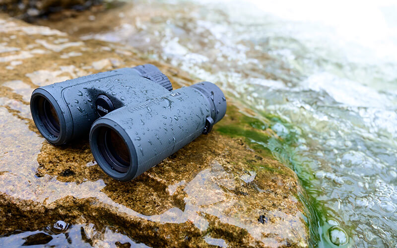 photo of a pair of PROSTAFF P7 10X30 binoculars on rocks by flowing water