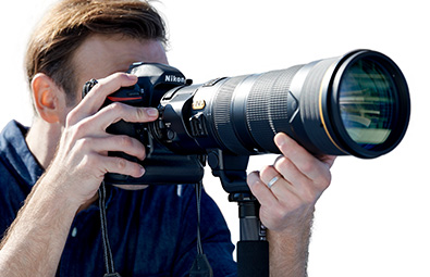 Photo of a photographer holding a camera and the AF-S NIKKOR 180-400mm f/4E TC1.4 FL ED VR lens