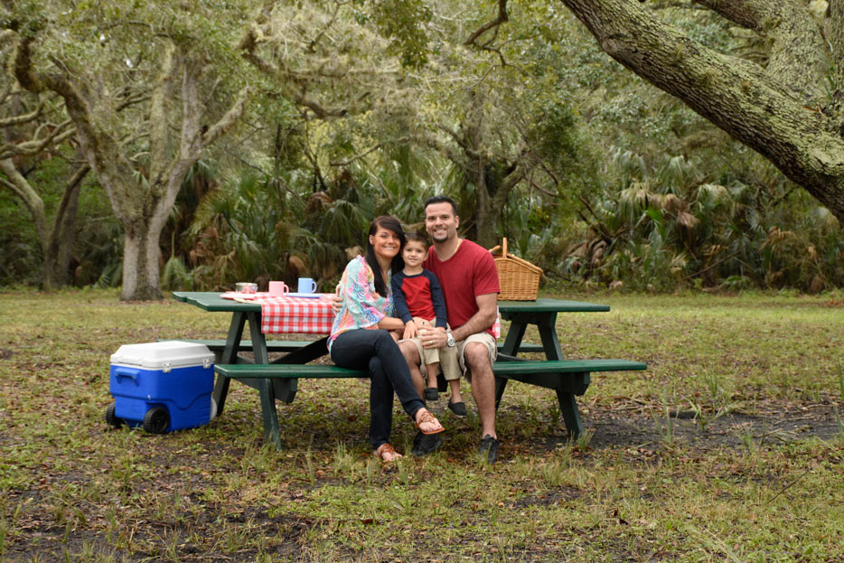 Fotografía tomada con el AF-S NIKKOR 50mm f/1.8G de un niño con sus padres haciendo un picnic bajo unos árboles