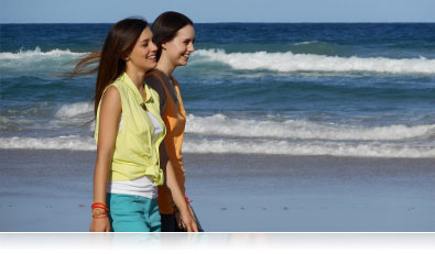 Two women walking along the shore with ocean waves in the background